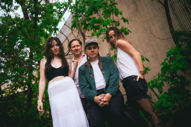 Four people standing in front of a tree, looking down at camera