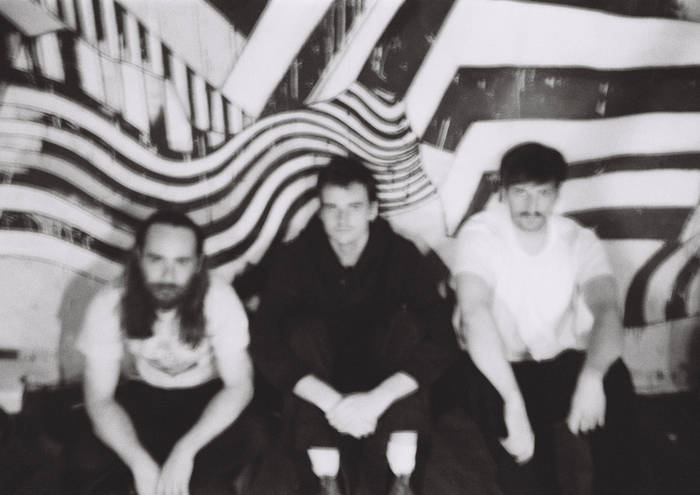 Black-and-white photograph of three people seated in front of a wavy, geometric striped backdrop.