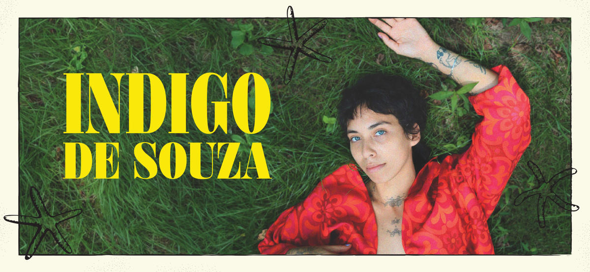 Artist Indigo De Souza laying down on green grass, with yellow text on the left side that reads "Indigo De Souza"