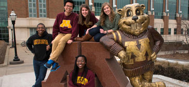 Students posing on the Goldy Statue outside of Coffman Memorial Union.